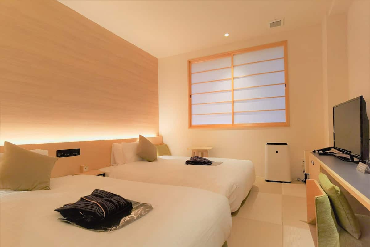 A hotel room with two beds, a desk, a television, and a small table.