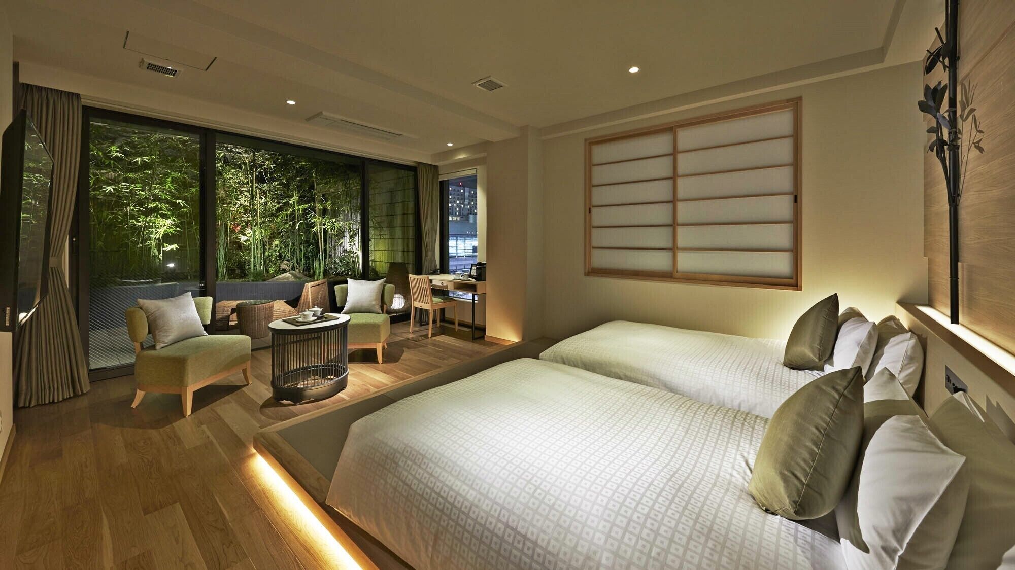 A modern hotel room with a large bed, a desk, a chair, and a view of greenery through the window.