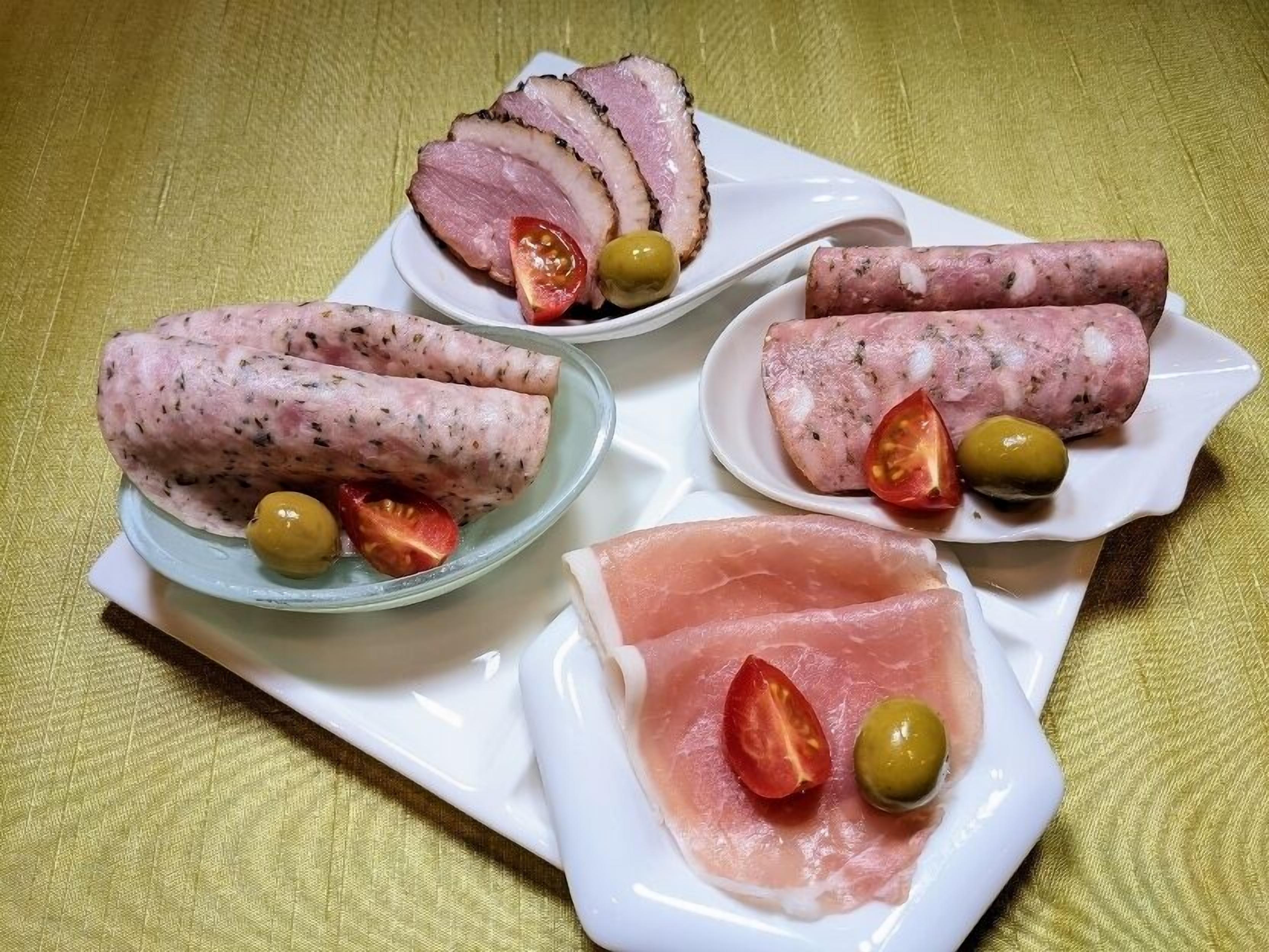 A variety of meat dishes including sliced ham, rolled meat, and thinly sliced meat, each accompanied by a cherry tomato and an olive.