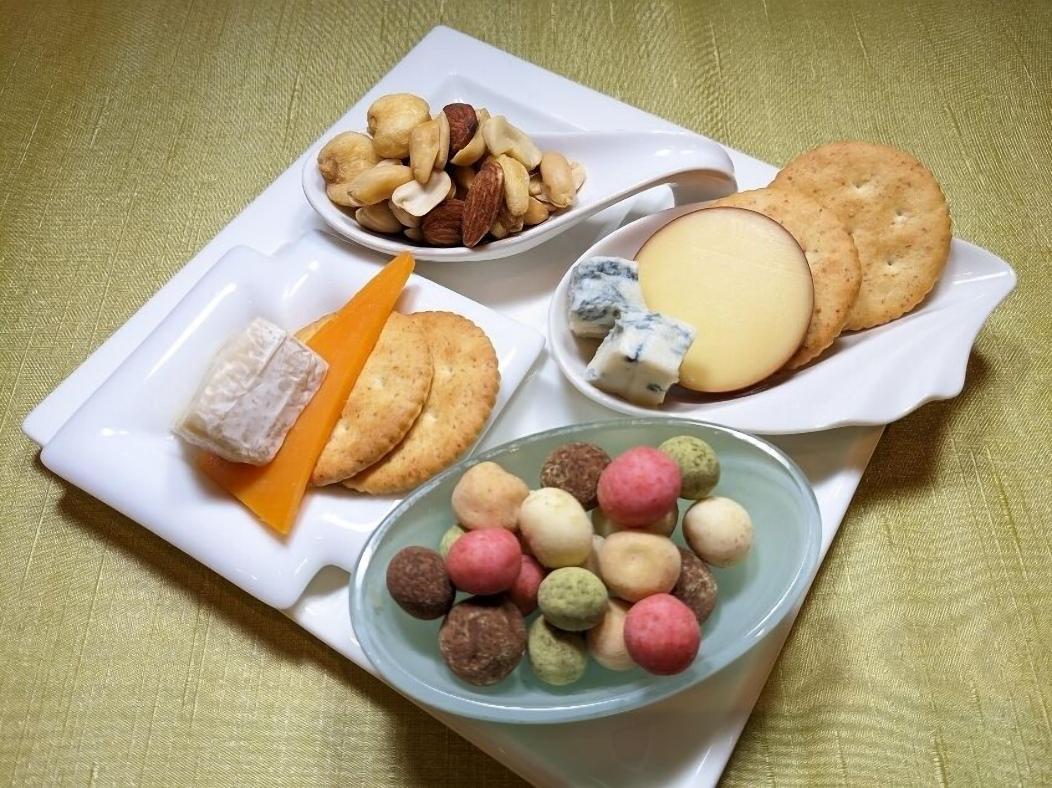 Une variété d’en-cas, notamment des noix, du fromage, des biscuits et des bonbons ronds et colorés, présentés sur un plateau blanc.