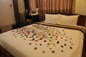 A neatly made bed with rose petals and a white towel arranged on it.