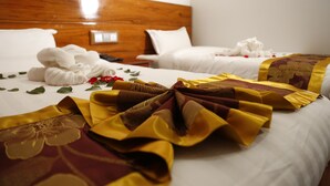 Habitación de hotel con dos camas, cada una con ropa blanca y cabeceros de madera. Se observan toallas y una manta decorativa sobre las camas.