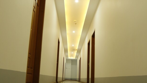 Un pasillo largo, bien iluminado, con piso reflectante, puertas de madera y techo con iluminación empotrada.