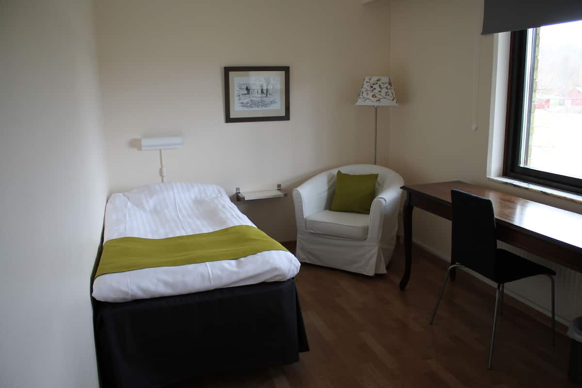 A small, clean room with a bed, a desk, a chair, and a window.