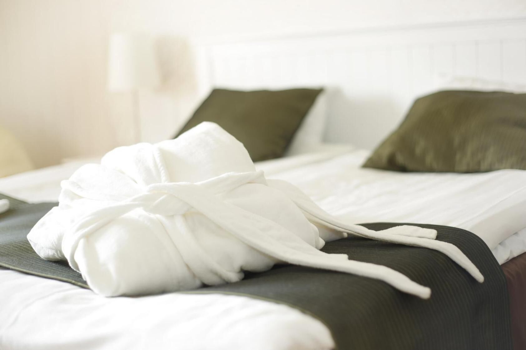 A neatly made bed with a white bathrobe on it, a green pillow, and a white pillow.