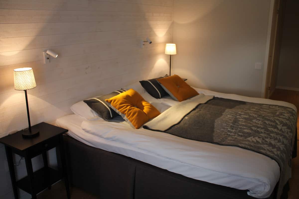 A neatly made bed with white bedding and multiple pillows, two bedside lamps, and a small wooden nightstand.