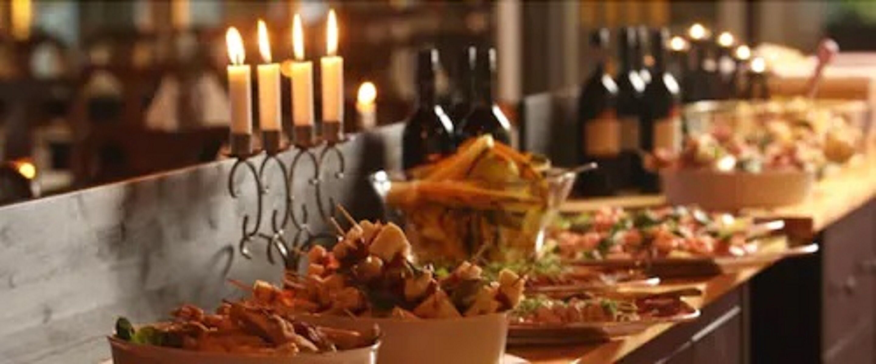 Mesa de buffet com diversos pratos e um castiçal com velas acesas.