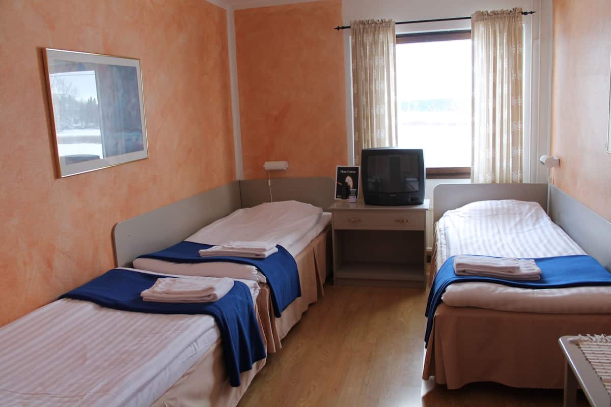 A hotel room with two single beds, a desk with a television, and a window with curtains.