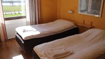 A hotel room with two single beds, a window with curtains, a painting on the wall, and a wooden floor.
