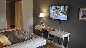 A hotel room with a bed, a desk, a chair, a TV mounted on the wall, and a lamp. - Yxnerum Hotell (Atvidaberg)