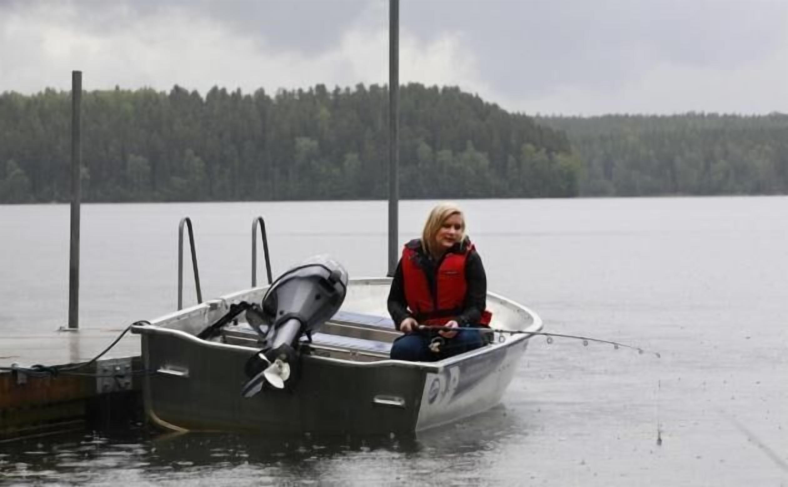 Una persona en un bote pequeño en un lago, con una orilla boscosa al fondo.
