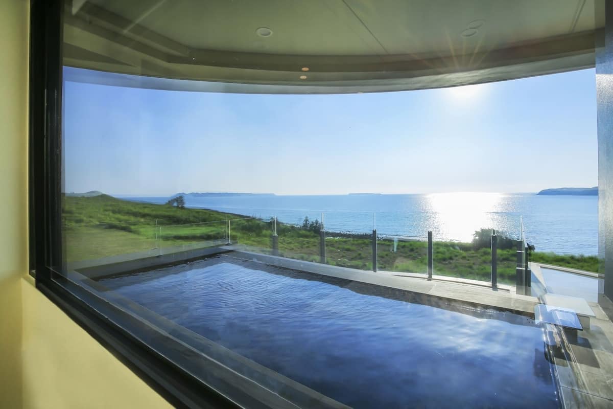 Une chambre moderne dotée d’une grande fenêtre donnant sur un plan d’eau et un paysage verdoyant.