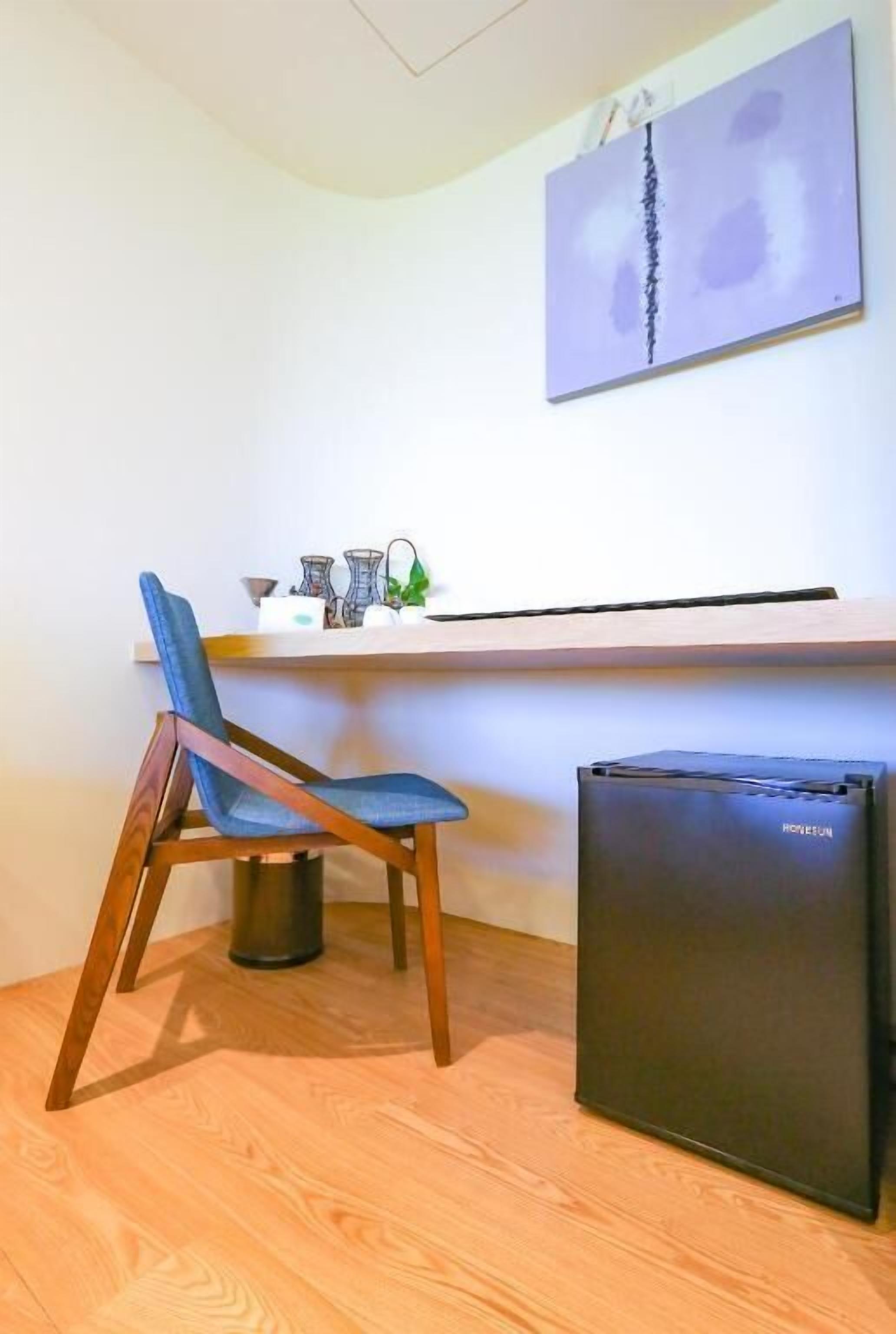 A compact workspace with a wooden chair, a small black refrigerator, and a white desk with a shelf holding various items.