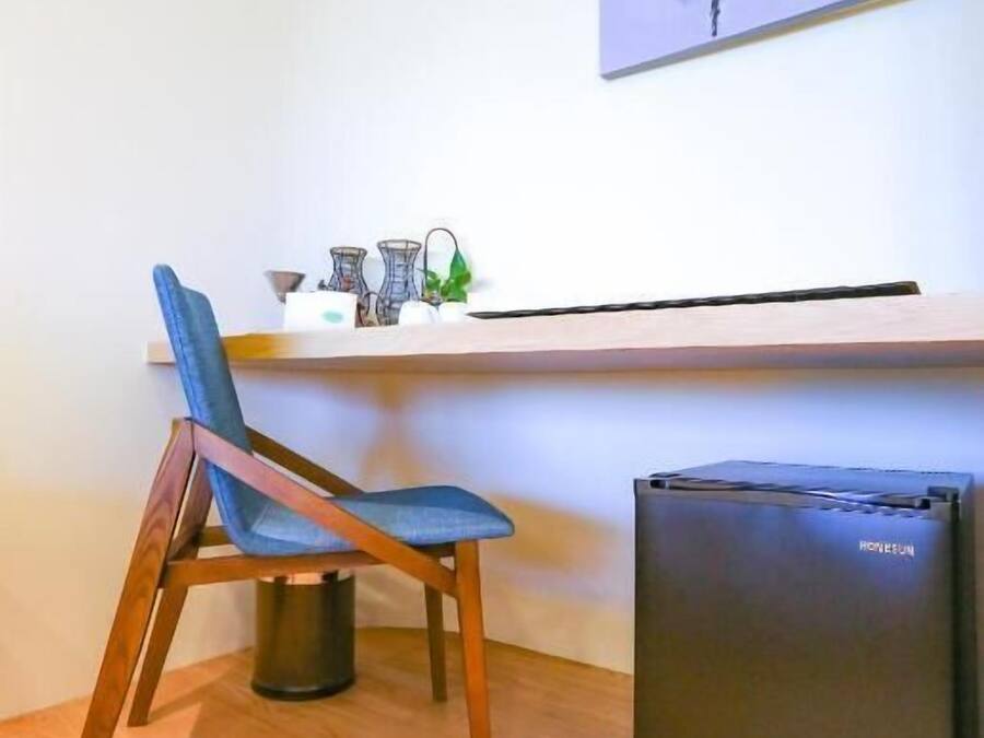 A compact workspace with a wooden chair, a small black refrigerator, and a white desk with a shelf holding various items.