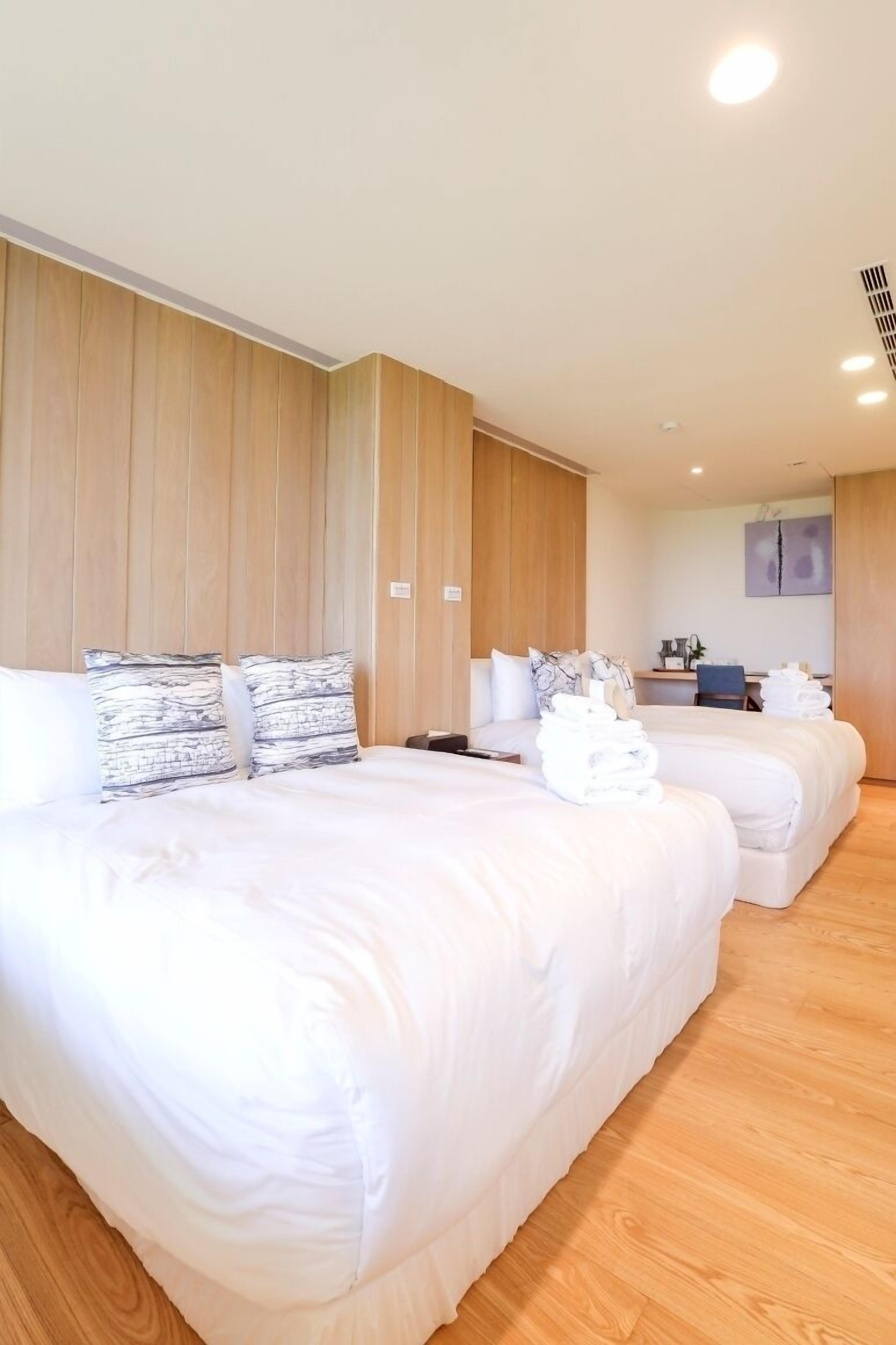 A hotel room with two beds, a wooden panel wall, a desk with a chair, and a bathroom.