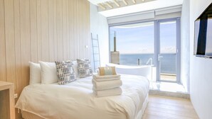 A modern bedroom with a large bed, a view of the sea, and a balcony with a chair. - Laguna Villas & Resorts (Magong)