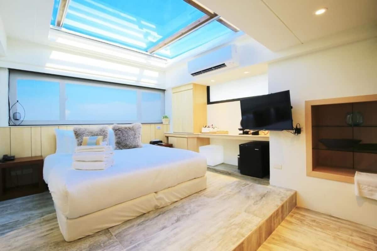 Une chambre moderne avec un grand lit, un téléviseur fixé au mur et une lucarne au plafond.