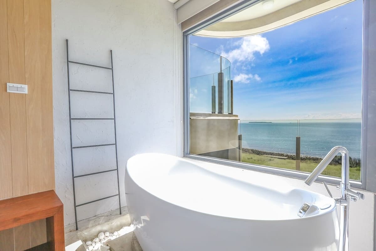 Une salle de bain moderne avec une baignoire sur pieds, une douche à parois de verre et une vue sur la mer.