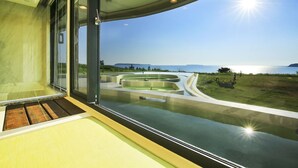 A modern hotel room with a large glass window offering a view of a landscaped garden and a body of water. - Laguna Villas & Resorts (Magong)