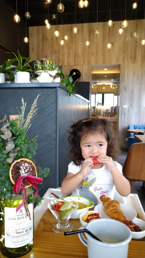 A child eating at a table with a bottle of Chateau Los Bollo chardonnay, a glass of water, and a croissant.