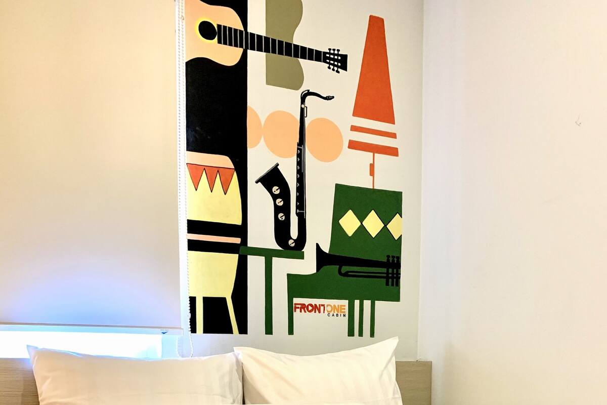 A neatly made bed with white linens in a room with a wall mural featuring musical instruments and the text "FRONTONE CABIN".