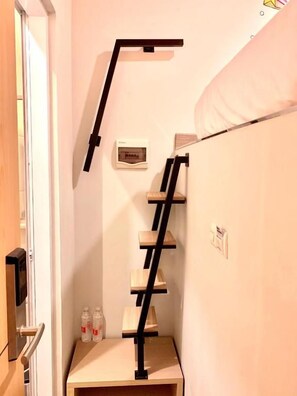 Una habitación estrecha con una estantería de madera y una escalera, una puerta y una pequeña mesa con botellas.