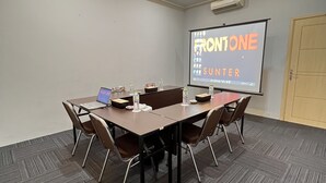A conference room with a large table, chairs, a projector screen displaying 'FRONTONE', and an air conditioning unit on the wall. - Front One Cabin Sunter (Jakarta)