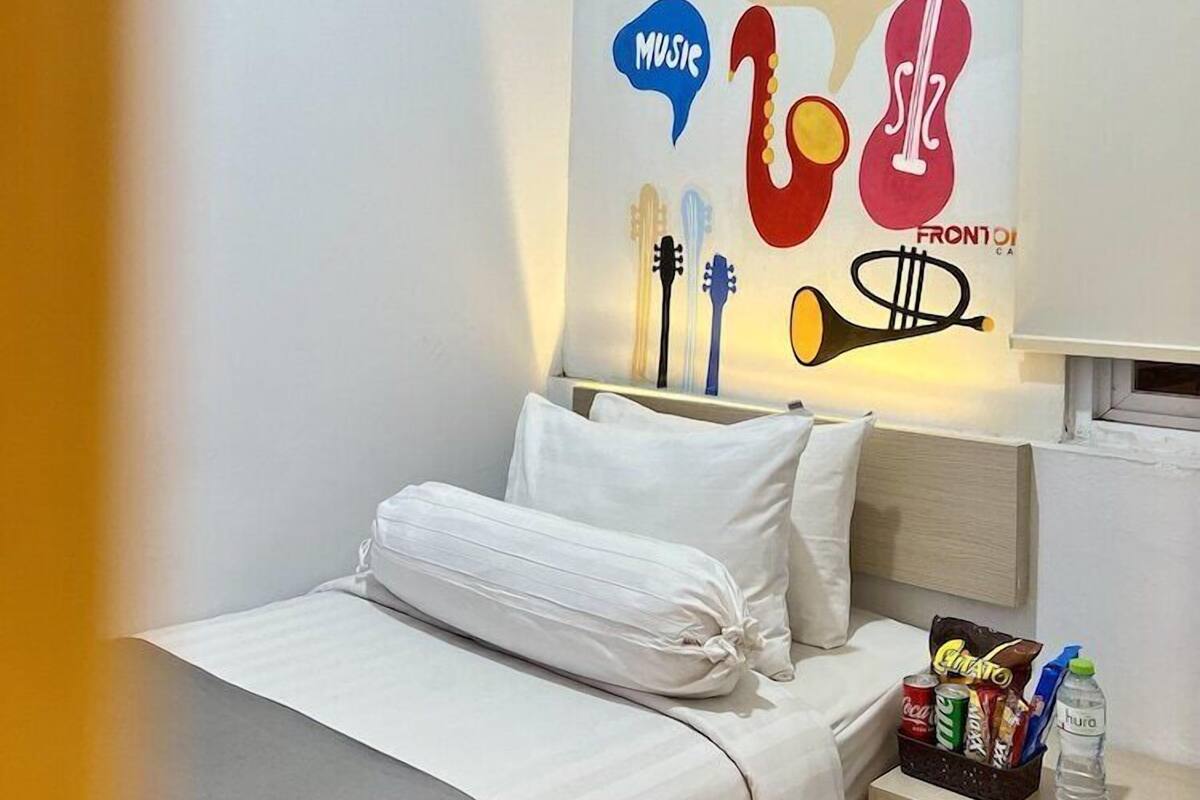 A hotel room with a bed, a bedside table with a water bottle, and a wall decoration featuring musical instruments and the word 'JAZZ'.