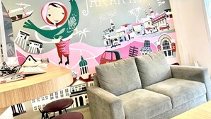 A room with a mural of Jakarta, a grey sofa, a wooden table with a keyboard, and two red chairs. - Front One Cabin Sunter (Jakarta)