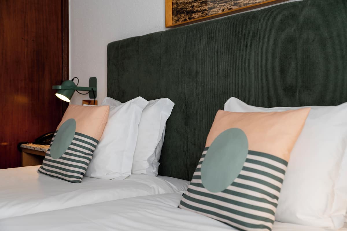 Een netjes opgemaakt bed met gestreepte kussens, een groen hoofdbord en een bedlampje.