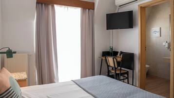 A hotel room with a bed, a desk with a chair, a television mounted on the wall, and a bathroom visible through an open door.