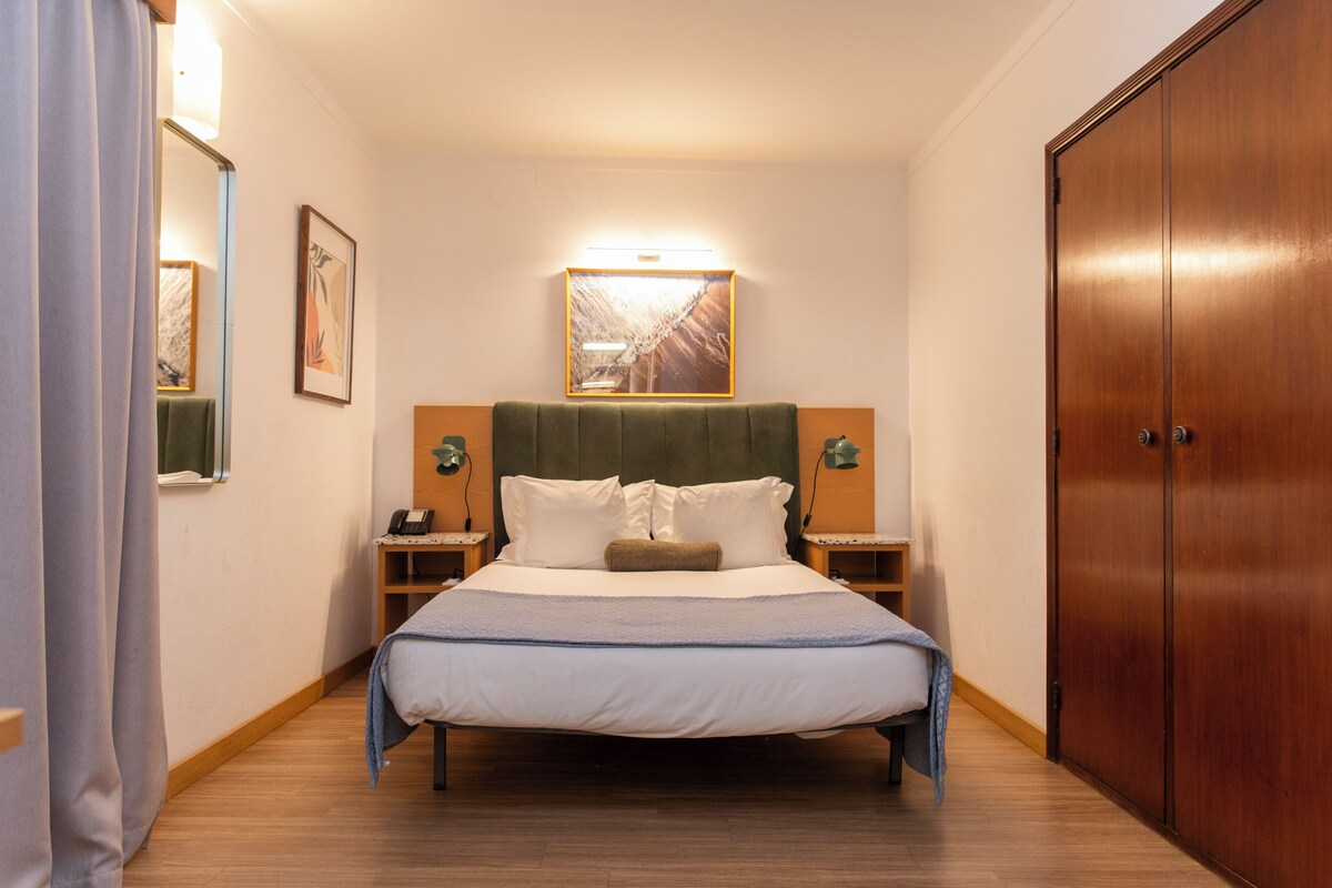 Una habitación de hotel con cama, mesitas de noche, armario y una obra de arte colgada en la pared.