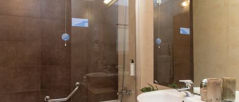 Un baño moderno con ducha envuelta en vidrio, un lavabo blanco y un mueble de tocador color beige.