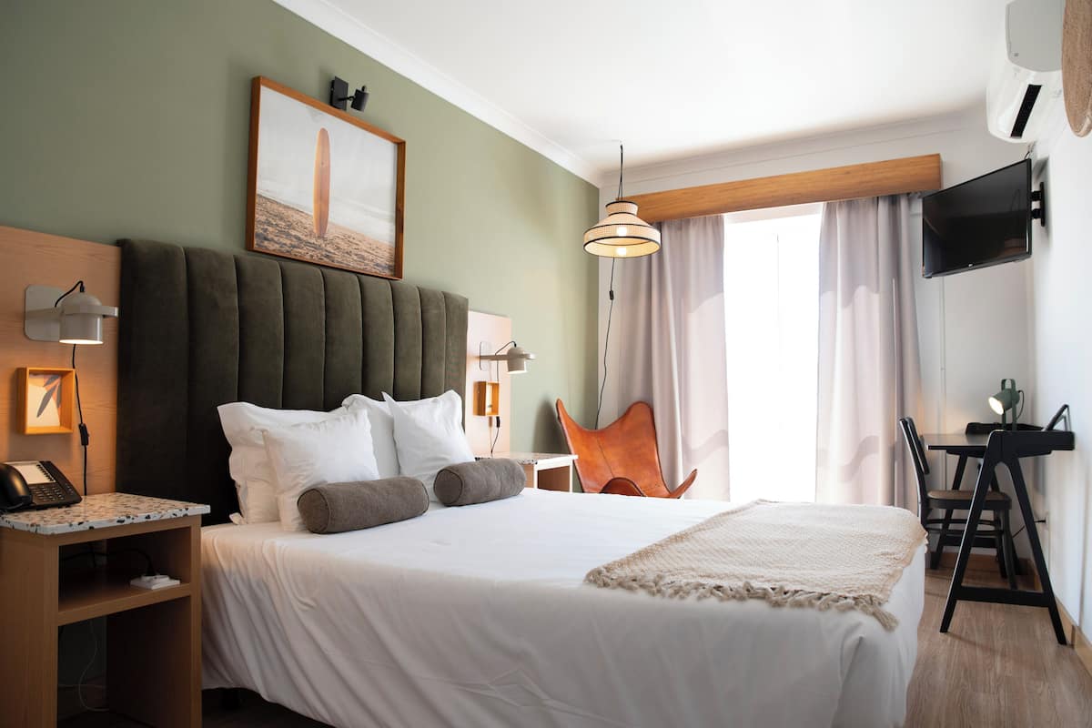 Een hotelkamer met een groot bed, een bureau, een stoel, een televisie en een schilderij aan de muur.