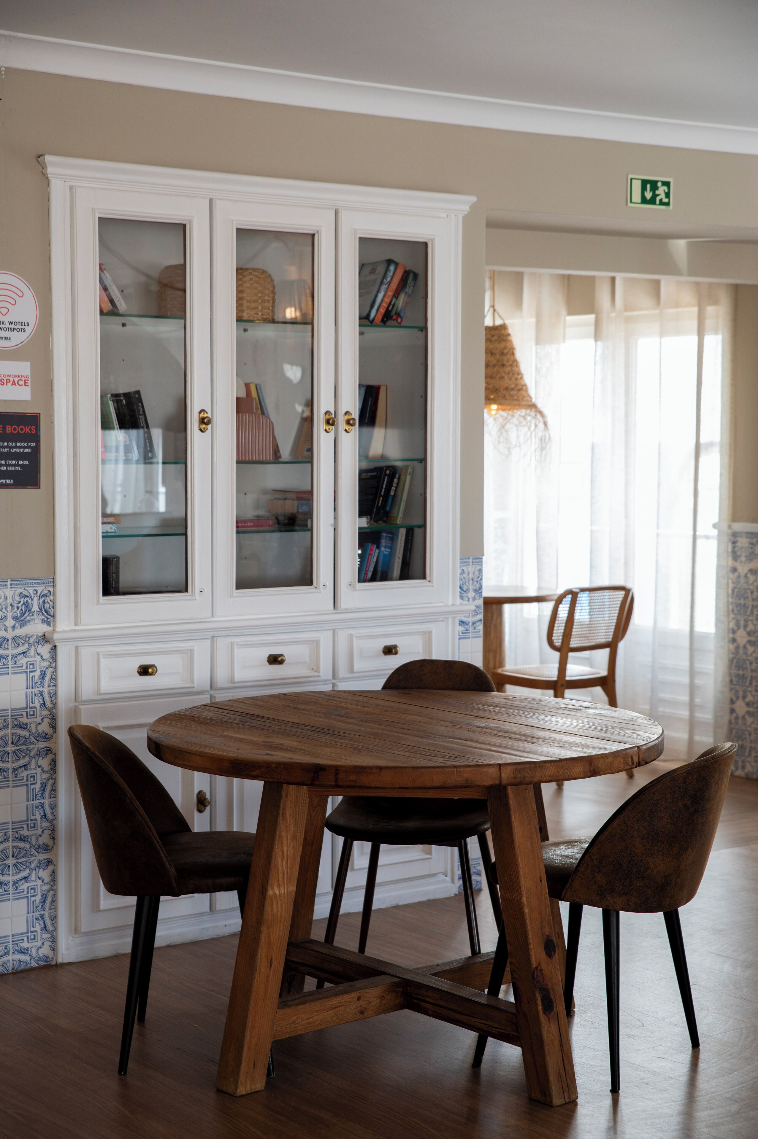 Un comedor con una mesa redonda de madera, cuatro sillas y un armario blanco con puertas de vidrio.