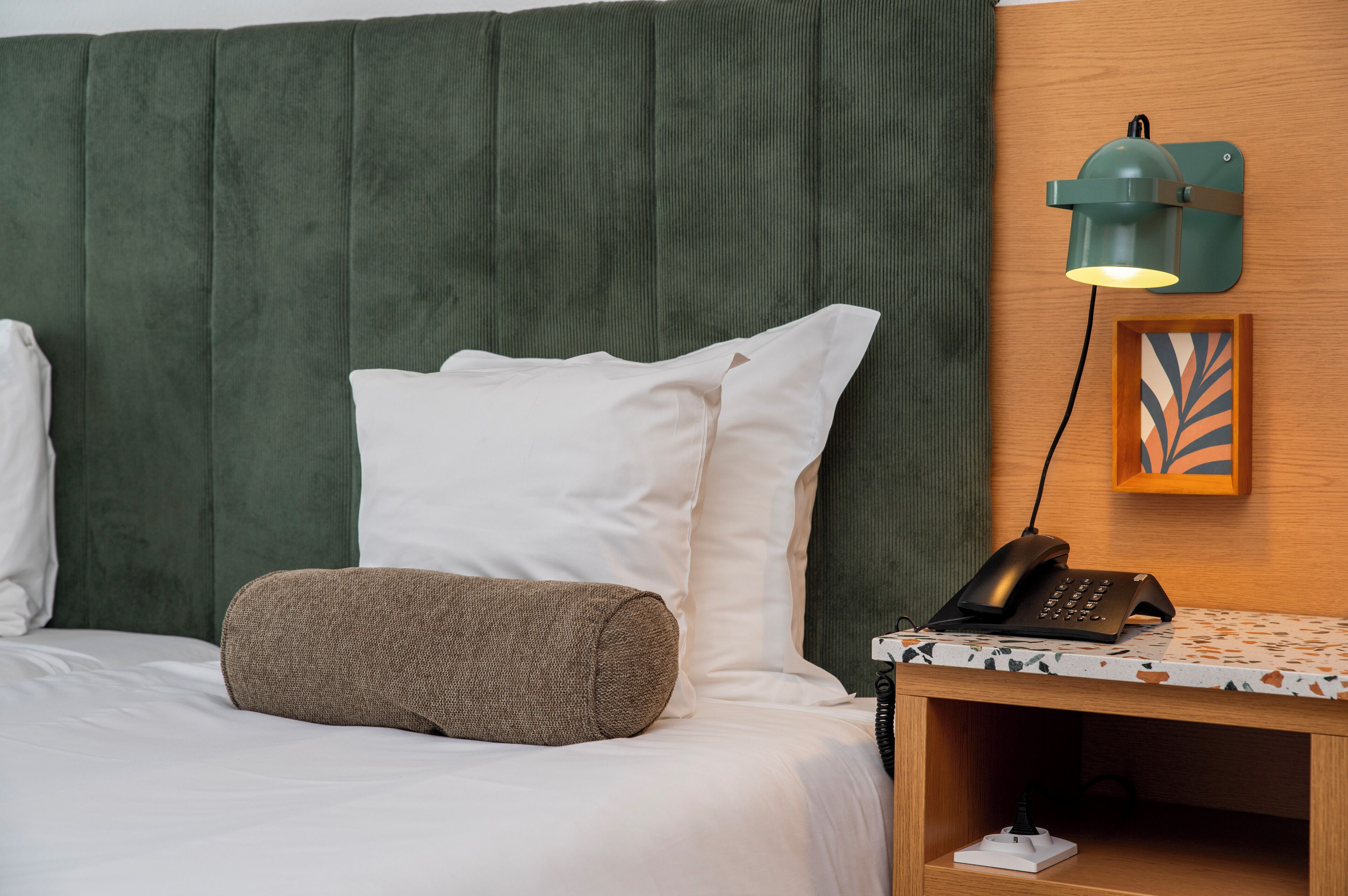 Une chambre d’hôtel avec un lit, des oreillers, une table de chevet avec une lampe, un téléphone et une œuvre d’art encadrée au mur.