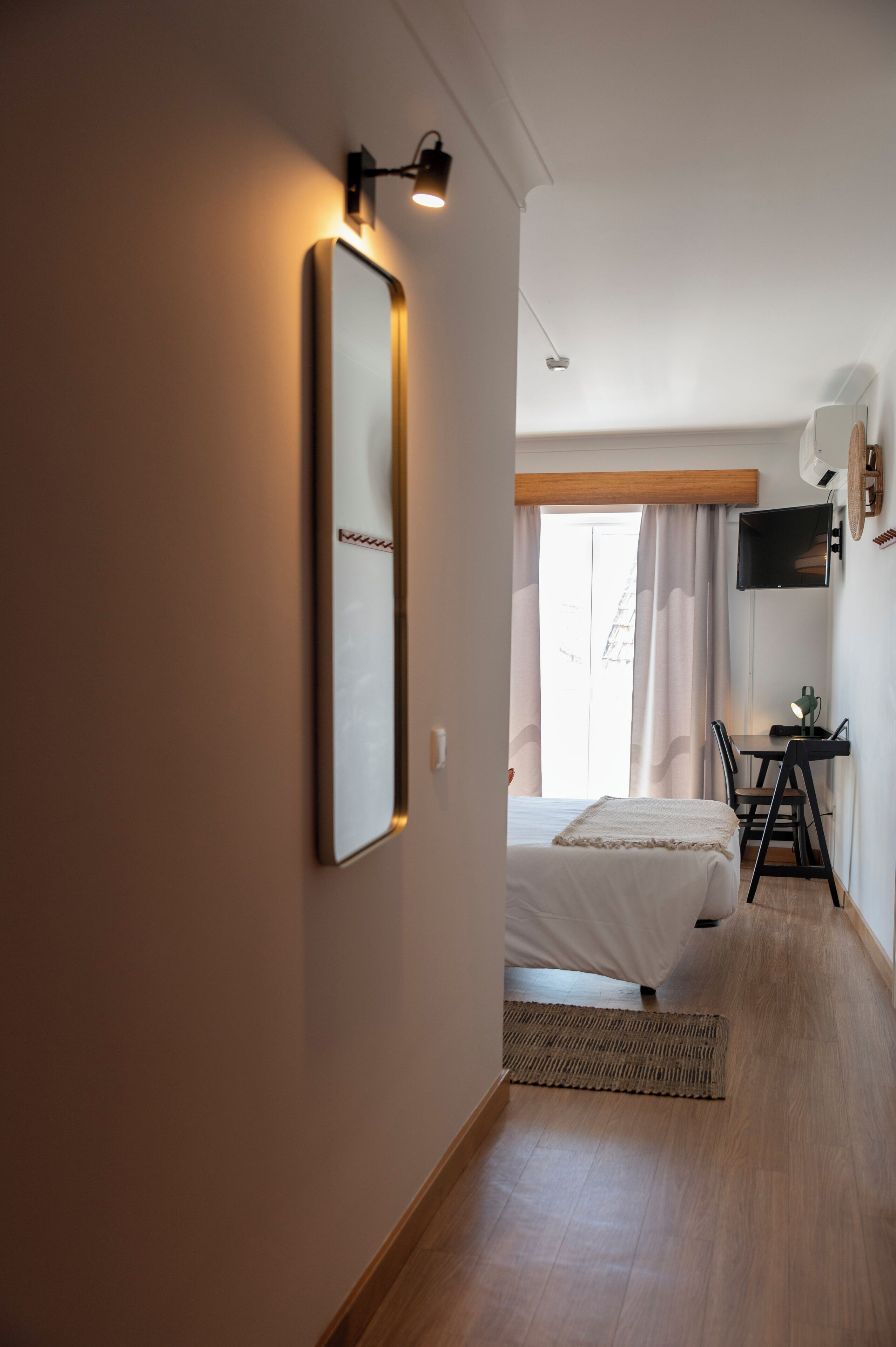 A hotel room with a bed, a desk, a chair, a flat-screen TV, and a large mirror on the wall.