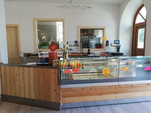 A bakery counter with a wooden counter, glass display case, and various baked goods. - Rosticaffè (Lavarone)