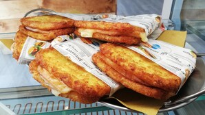 Una bandeja con alimentos fritos, probablemente sándwiches, envueltos en papel de periódico.