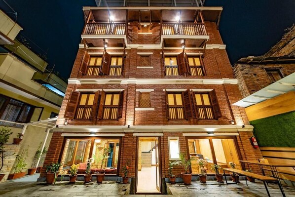 A multi-story building with a brick facade, balconies, and a courtyard with potted plants.