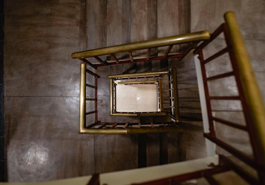 Uma escada de madeira com corrimão de metal e uma parede branca no topo.