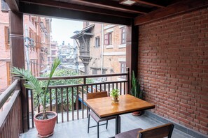 A balcony with a wooden table, chairs, and a potted plant. - Traditional Stay (Lalitpur)