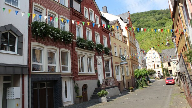 A row of traditional European townhouses with red brick facades, white window frames, and a street decorated with colorful bunting. - Haus Budinger Ferienwohnung Appartements (Alf)