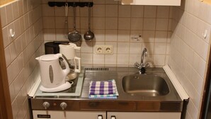 A compact kitchen with a built-in stove, sink, and white cabinets. - Haus Budinger Ferienwohnung Appartements (Alf)