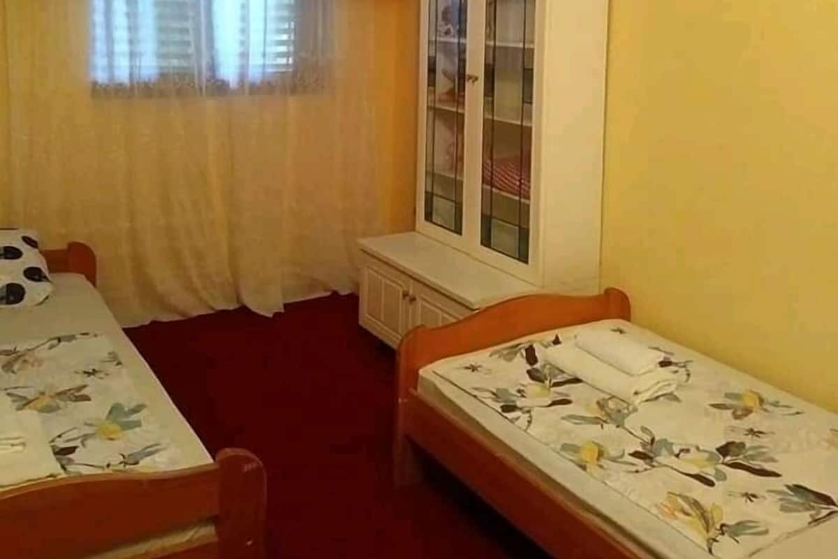 Quarto com duas camas de solteiro, uma cama beliche de madeira, um armário com portas de vidro, uma janela com cortinas e um tapete vermelho.