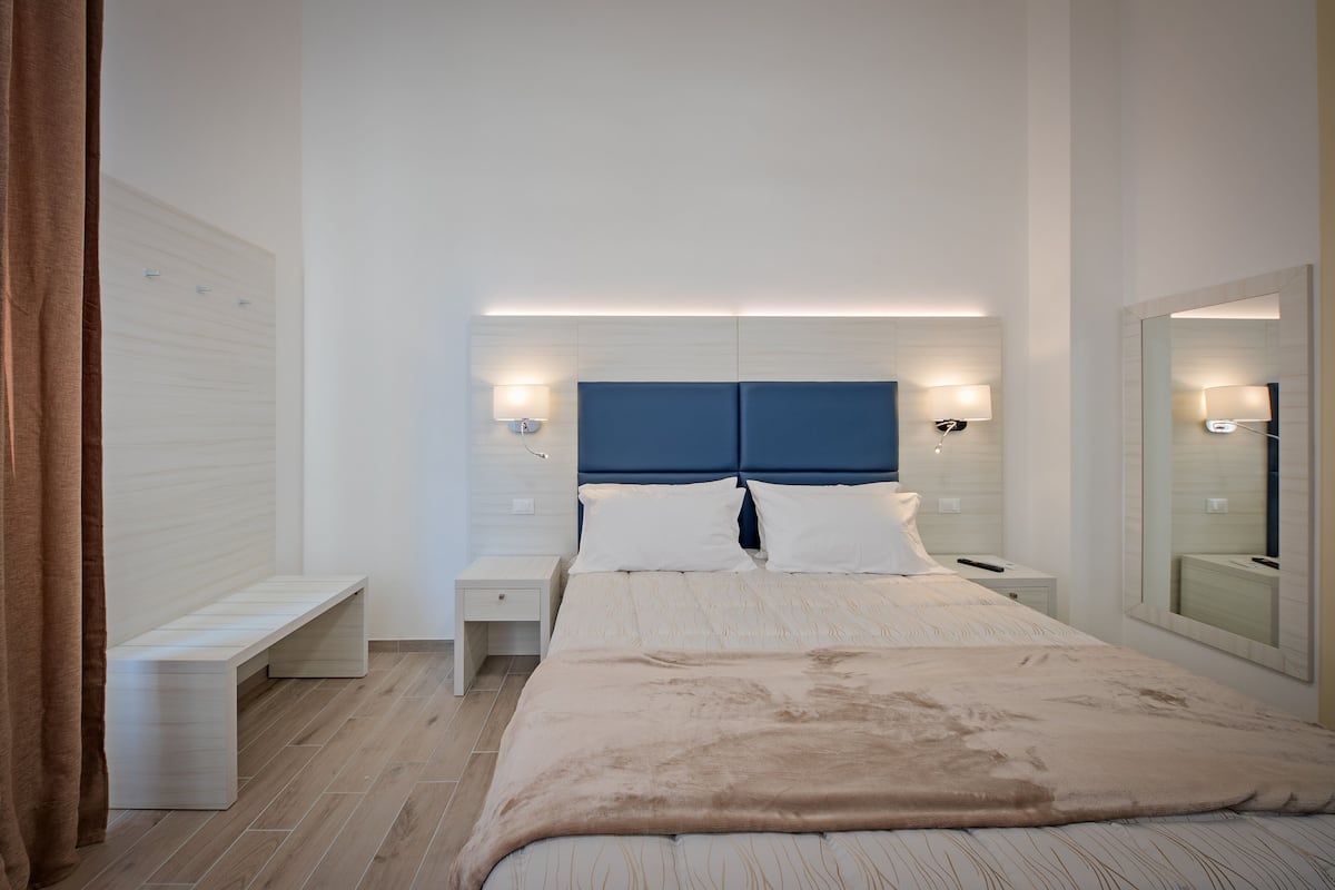 A modern bedroom with a large bed, bedside tables, a bench, and a mirror.