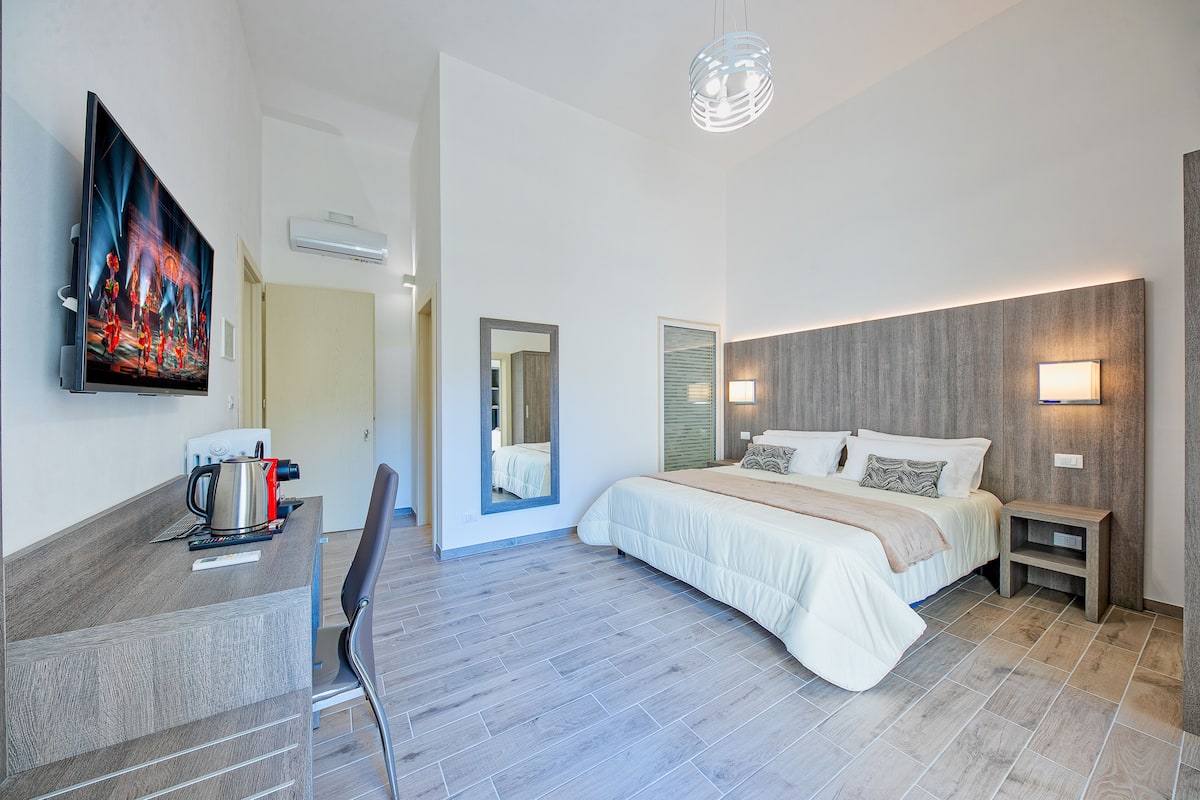 A modern hotel room with a bed, bedside table, and a flat-screen TV mounted on the wall.