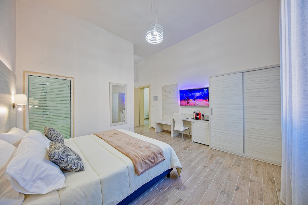 A modern hotel room with a large bed, a desk, and a TV.