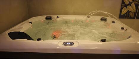 Un jacuzzi con panel de control, rodeado por un banco de madera.