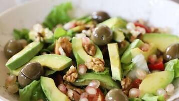 A bowl of salad with avocado, walnuts, and pomegranate seeds.